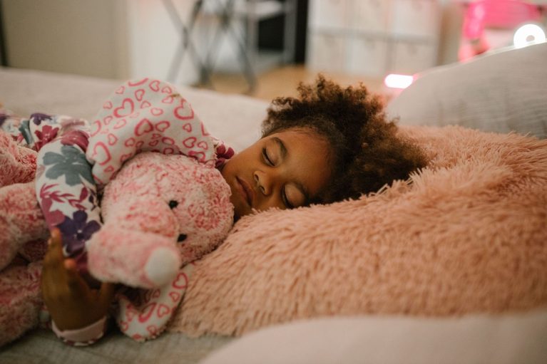A young girl sleeping peacefully with a pink stuffed animal in a cozy bedroom environment