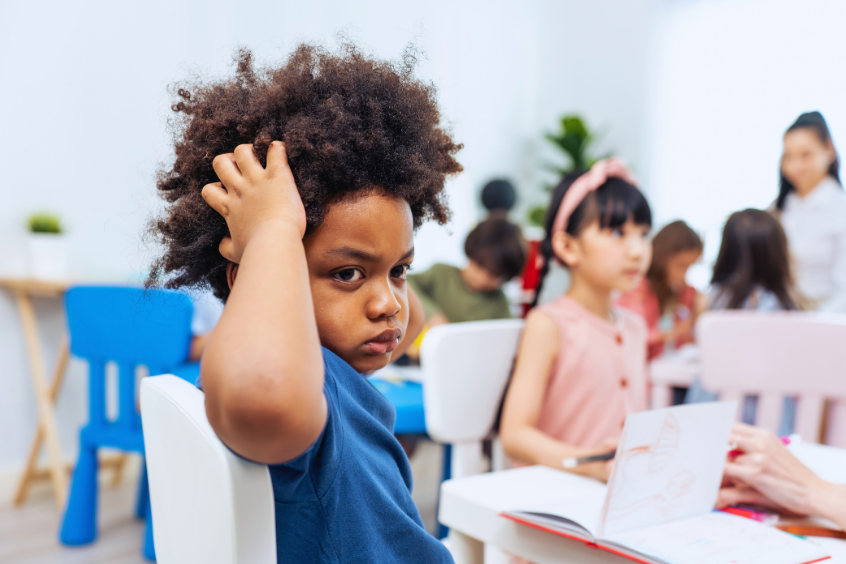 Portrait of an African-American child sitting in a preschool classroom looking uncomfortable